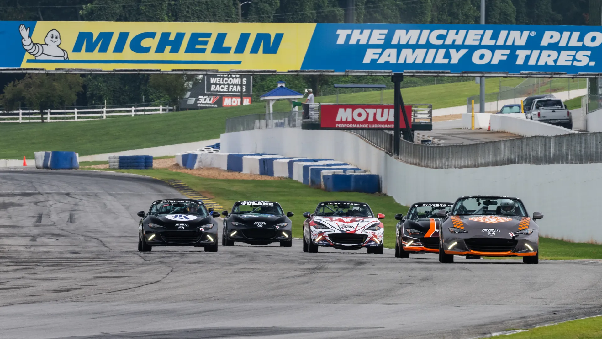 Five Collegiate Racing Series Mazda MX-5s spread across the track beneath the Michelin bridge at Michelin Raceway Road Atlanta.